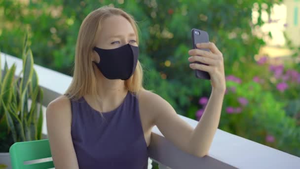 ティッシュ・フェイスのマスクをした若い女性がスマートフォンで話しかける。おしゃれなフェイスマスク。社会的距離概念 — ストック動画