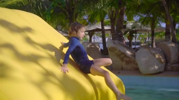 Niño pequeño en una carrera de obstáculos inflable en un parque acuático. Concepto de verano. Disparo en cámara lenta — Vídeos de Stock