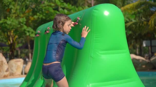 Niño pequeño en una carrera de obstáculos inflable en un parque acuático. Concepto de verano. Disparo en cámara lenta — Vídeos de Stock