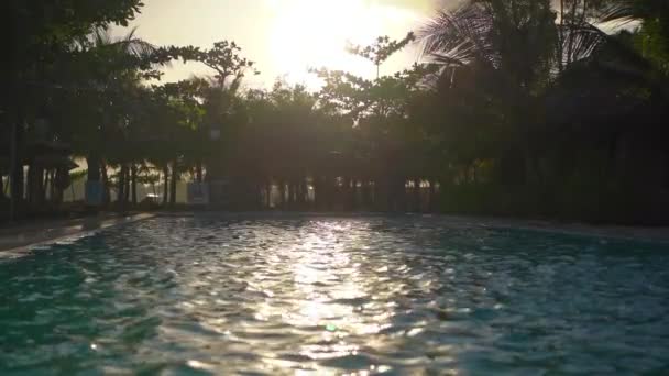 Handheld shot of a swimming pool in tropical surrounding during sunset. Slowmotion shot — Stock Video