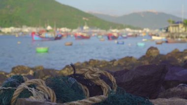 Arka planda Asyalı bir balıkçı köyü olan kayalık deniz kıyısında yatan plastik çöpler. Plastik kirliliği kavramı.