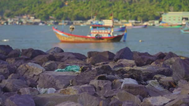 Műanyag szemét feküdt a sziklás tengerparton egy ázsiai halász falu a háttérben. Műanyagszennyezés fogalma — Stock videók