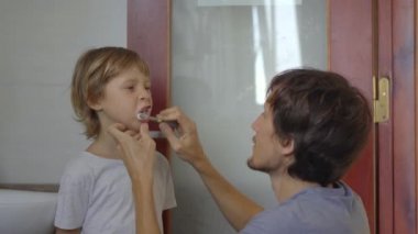 Bir adam küçük oğluna dişlerini fırçalar. Diş bakımı konsepti