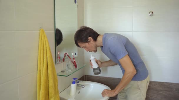 Een jonge man gebruikt een draagbare water flosser tandheelkundige orale Irrigator om zijn tanden schoon te maken — Stockvideo