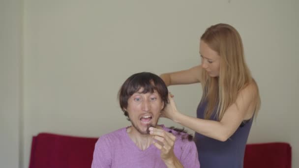Egy fiatal nő levágja a haját a barátjának vagy a férjének a zárlat miatt. Próbálja követni a videó utasításokat. Az ember fél, hogy szörnyű lesz a frizurája. Társadalmi elszigeteltség — Stock videók
