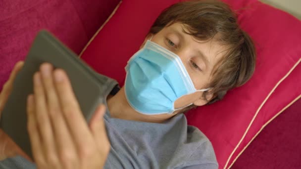 E-book e formazione online. Un uomo sta leggendo un libro elettronico a casa durante la quarantena. Un uomo con una maschera medica è rimasto a casa in isolamento — Video Stock