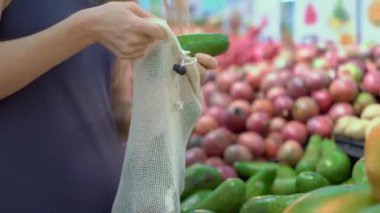 Bir kadın markette tekrar kullanılabilir mendil torbasına avokado koyar. Plastik atık kavramını küçült
