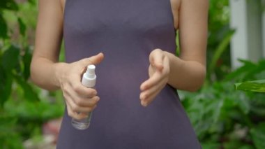 Genç bir kadın, bir sokakta ayakta duran ellerine sprey sıkacak şekilde dezenfektan sürüyor. Sosyal uzaklık kavramı. Dezenfeksiyon kavramı