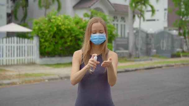 Eine junge Frau trägt ein Desinfektionsmittel in Form eines Sprays auf ihre Hände auf, die auf einer Straße stehen. Soziale Distanzierung. Desinfektionskonzept — Stockvideo