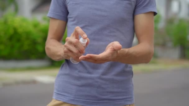 Un jeune homme applique un désinfectant sous forme de spray sur sa main debout sur une rue. Concept de distance sociale. Concept de désinfection — Video