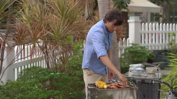 Ein junger Mann kocht Gemüse und Garnelen auf einem Grill in seinem Hinterhof — Stockvideo