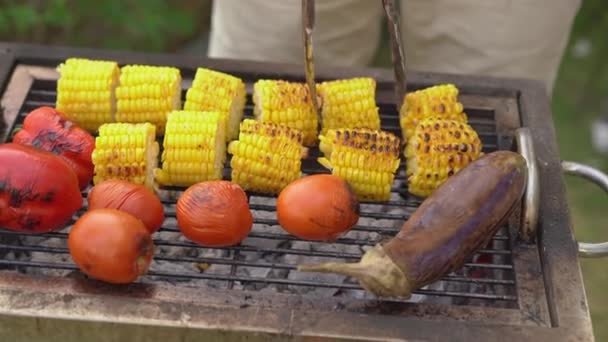 En ung man lagar grönsaker och räkor på en grill i trädgården. — Stockvideo