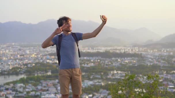 Een jonge man toerist maakt een selfie op de miuntaing met uitzicht op de Nha Trang stad, een beroemde toeristische bestemming in Vietnam — Stockvideo