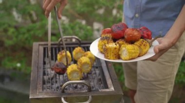 Genç bir adam arka bahçesindeki barbeküde karides ve sebze pişiriyor.