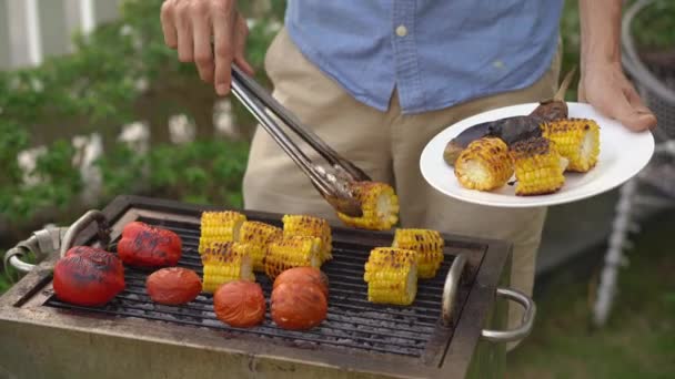 Молодий чоловік готує овочі та креветки на барбекю на задньому дворі — стокове відео