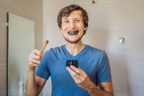 Young man brush teeth using Activated charcoal powder for brushing and whitening teeth. Bamboo eco brush