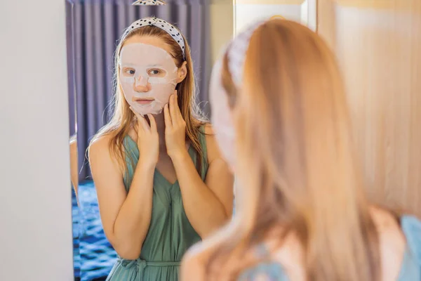 Giovane donna dai capelli rossi che fa foglio maschera facciale. Concetto di bellezza e cura della pelle — Foto Stock