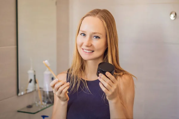 Молодая женщина чистит зубы черной зубной пастой с активным углем и черной зубной щеткой в ванной комнате — стоковое фото