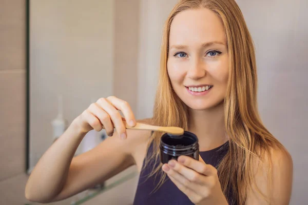 Молодая женщина чистит зубы черной зубной пастой с активным углем и черной зубной щеткой в ванной комнате — стоковое фото