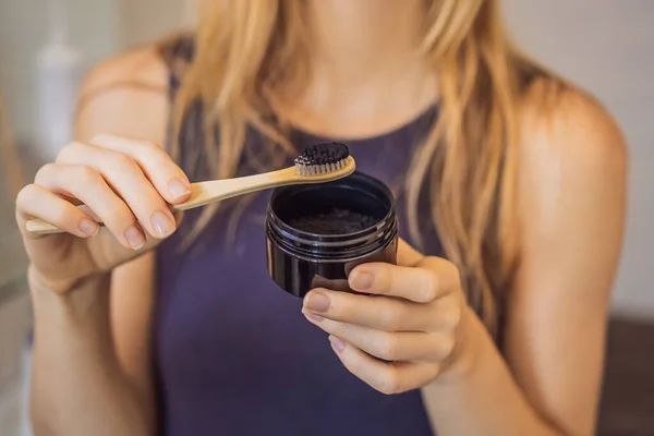 Νεαρή γυναίκα βουρτσίζει τα δόντια της με μαύρη οδοντόκρεμα με ενεργό άνθρακα, και μαύρη οδοντόβουρτσα στο μπάνιο της — Φωτογραφία Αρχείου