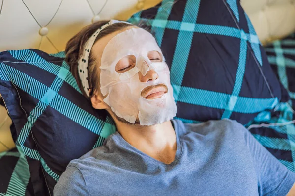 Young Man Doing Facial Mask Sheet. Concepto de belleza y cuidado de la piel —  Fotos de Stock