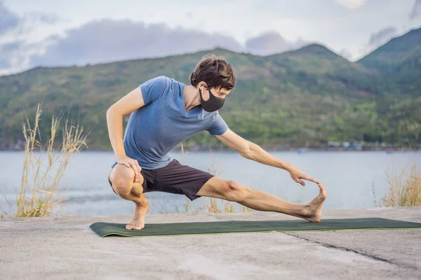 Young man in medical mask performing some workouts in the park during coronavirus quarantine, Coronavirus pandemic Covid-19. Sport, Active life in quarantine surgical sterilizing face mask protection