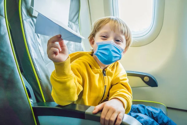 小男孩在度假的商业喷气式飞机上玩纸飞机，游客们害怕2019年的ncov病毒。医疗蒙面游客 — 图库照片