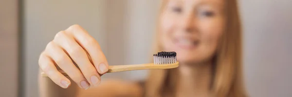 Joven mujer cepillarse los dientes con una pasta de dientes negro con carbón activo, y cepillo de dientes negro en su cuarto de baño BANNER, FORMATO LARGO — Foto de Stock