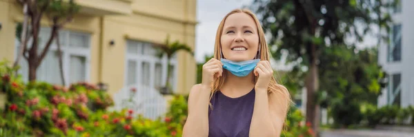 Quarantine is over concept. Woman taking off mask against the background of small town houses. We are safe. Coronavirus ended. We won. No more quarantine. Breathe deep. Take off the mask. Coronavirus — Stock Photo, Image