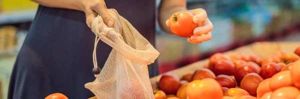 Una mujer elige tomates en un supermercado sin usar una bolsa de plástico. Bolsa reutilizable para comprar verduras. Concepto de cero residuos BANNER, FORMATO LARGO — Foto de Stock