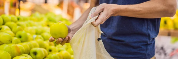 De mens kiest appels in een supermarkt zonder gebruik te maken van een plastic zak. Herbruikbare tas voor het kopen van groenten. Geen afval concept BANNER, LANG FORMAT — Stockfoto