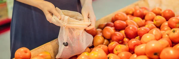 Een vrouw kiest tomaten in een supermarkt zonder een plastic zak te gebruiken. Herbruikbare tas voor het kopen van groenten. Geen afval concept BANNER, LANG FORMAT — Stockfoto