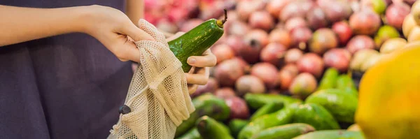 Woman chooses avocado in a supermarket without using a plastic bag. Reusable bag for buying vegetables. Zero waste concept BANNER, LONG FORMAT — Stock Photo, Image