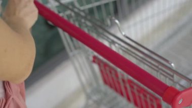 Genç bir kadın enfeksiyondan korunmak için market arabasının sapını dezenfekte ediyor. Sosyal uzaklık kavramı. Kapsamlı koruma kavramı.