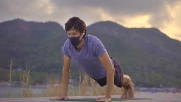 A young man wearing a protective face mask does physical training on a river or seaside. Physical activity during the quarantine. Covid-19 outbreak — Stock Video