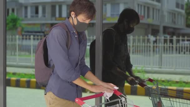 Młody człowiek dezynfekuje uchwyt wózka w supermarkecie, by chronić się przed kontaktem z infekcją. Koncepcja dystansu społecznego. Koncepcja ochrony przeciwżylakowej. — Wideo stockowe