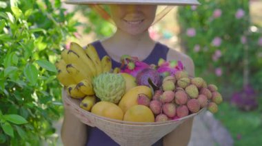 Vietnam şapkasındaki çeşitli meyveler. Vietnam şapkalı kadın elinde tropikal meyvelerle dolu bir şapka daha tutuyor.
