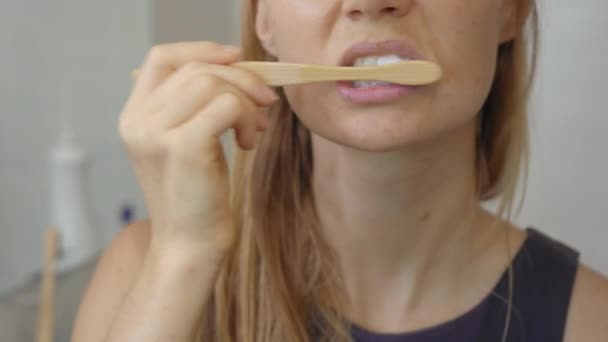 Uma jovem escova os dentes com uma escova de madeira de bambu. Zero conceito de desperdício. Conceito de produtos biodegradáveis — Vídeo de Stock