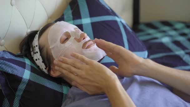 Un jeune homme allongé sur un lit avec un masque cosmétique sur le visage. Concept de soins de la peau — Video