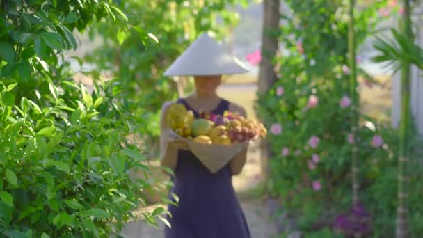 Vielfalt an Früchten in einem vietnamesischen Hut. Frau mit vietnamesischem Hut hält einen weiteren Hut voller tropischer Früchte in der Hand — Stockvideo