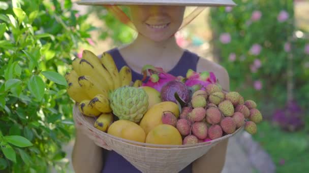 Vielfalt an Früchten in einem vietnamesischen Hut. Frau mit vietnamesischem Hut hält einen weiteren Hut voller tropischer Früchte in der Hand — Stockvideo