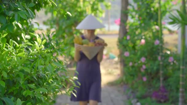 Vielfalt an Früchten in einem vietnamesischen Hut. Frau mit vietnamesischem Hut hält einen weiteren Hut voller tropischer Früchte in der Hand — Stockvideo