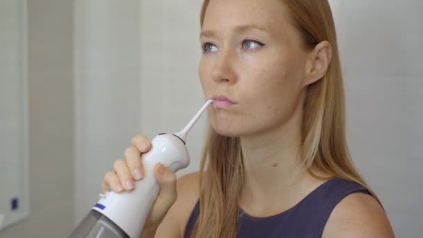 Een jonge vrouw gebruikt een draagbare water flosser orale Irrigator om haar tanden te reinigen. Tandverzorging concept — Stockvideo