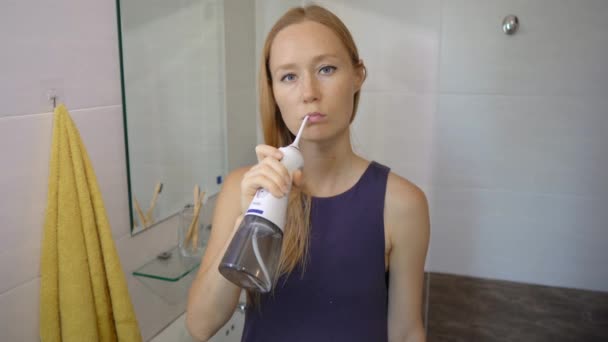 A young woman uses a portable water flosser dental oral Irrigator to clean her teeth. Teeth care concept — Stock Video