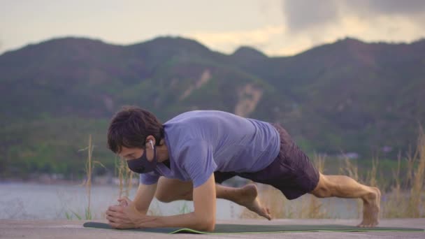 Ein junger Mann mit einer schützenden Gesichtsmaske macht körperliches Training an einem Fluss oder am Meer. Körperliche Aktivität während der Quarantäne Covid-19-Ausbruch — Stockvideo