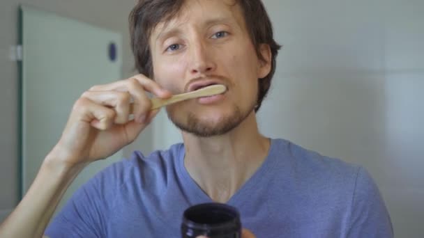 Genç bir adam diş beyazlatmak için kömür kullanarak bambu ağacından yapılmış bir fırçayla dişlerini fırçalıyor. Sıfır atık. Biyolojik çözünebilir ürünler konsepti — Stok video