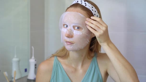 Een jonge vrouw zet een cosmetisch gezichtsmasker op. Huidverzorgingsconcept — Stockvideo