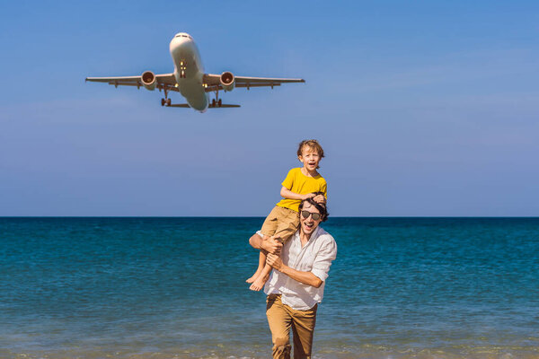Coronavirus is over. Quarantine weakened. Take off the mask. Now you can travel. Dad and son have fun on the beach watching the landing planes. Traveling on an airplane with kids concept. Text space