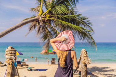 Coronavirus bitti. Karantina zayıfladı. Maskeni çıkar. Artık seyahat edebilirsin. Tropikal adada tatil. Şapkalı kadın ahşap köprüden deniz manzarası seyrediyor.