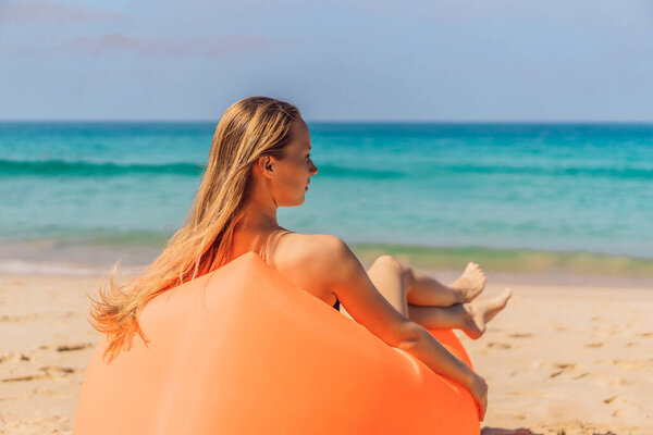 Coronavirus is over. Quarantine weakened. Take off the mask. Now you can go to public places. Summer lifestyle portrait of pretty girl sitting on the orange inflatable sofa on the beach of tropical